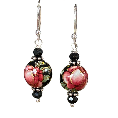 a black round vintage bead is painted with a red rose and green leaves and hanging from sterling silver ear wires and bordered by small black roundel beads and silver spacers