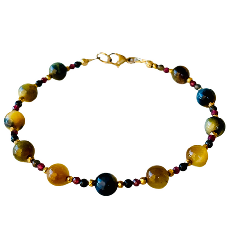 A beaded bracelet is shown with round tigers eye stones in varying shades of beige and blue, alternating with smaller beads of red garnet, blue tigers eye, and gold.