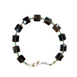 Necklace with black square beads and gold chain on a gray background