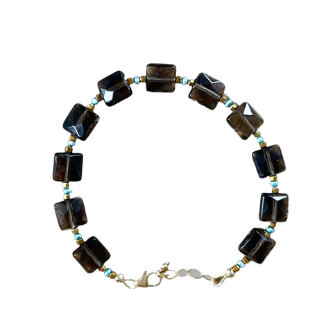 Necklace with black square beads and gold chain on a gray background