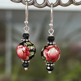 a black round vintage bead is painted with a red rose and green leaves and hanging from sterling silver ear wires and bordered by small black roundel beads and silver spacers